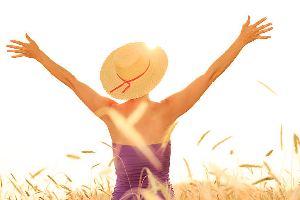 Rear view of woman in wheat field with arms outstretched.