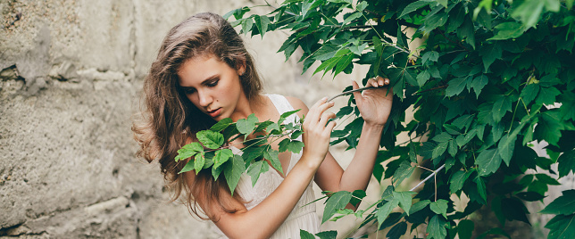 Beautiful happy girl with curly natural hair in white dress near green tree leaves. Summer beauty portrait. Dreamer lady enjoy nature. Inspired woman with dreamy sight in long tunnel in forest.