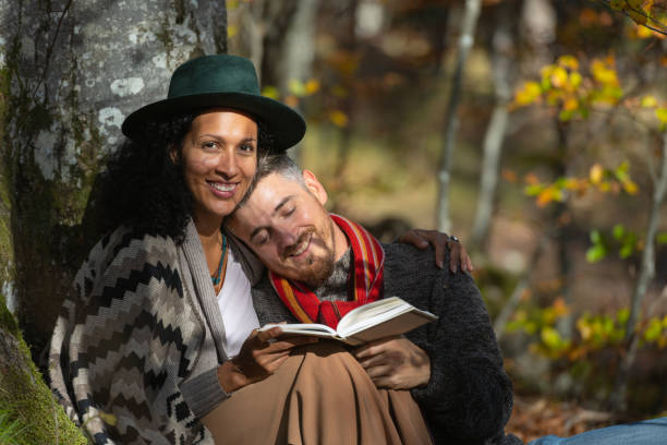 A couple in love is sitting in the forest with a book.