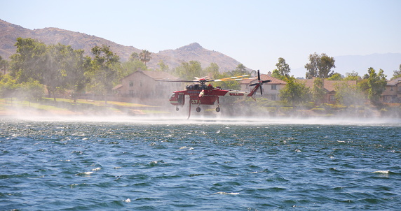 Cal Fire helicopter fills up from a lake to fight nearby fire.  Shot in Moreno Valley, California in July of 2023.
