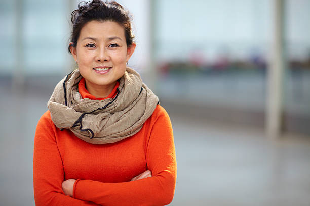 portrait of one mature Chinese woman picture of one mature Chinese woman looking at camera smile with arms crossed indoor scarf photos stock pictures, royalty-free photos & images