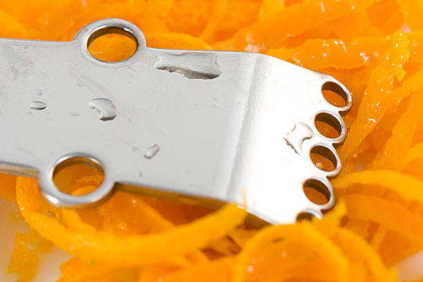 Stainless steel citrus grater on thin curls of orange stock photo