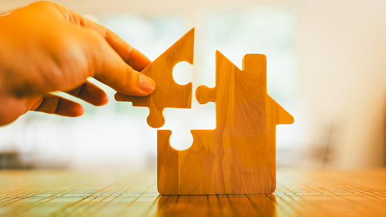 Hand Holding the Key to Real Estate: Unlocking Property Dreams with a House Puzzle.