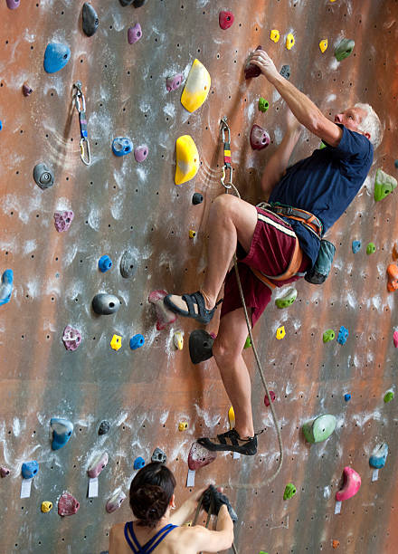 Senior Man Indoor Rock Climbing Fit senior man climbing an inverted rock wall. crag stock pictures, royalty-free photos & images