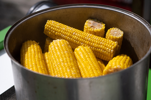 A street vendor cooks corn in a pot and sells it. Lots of sweet, delicious and boiled corn.