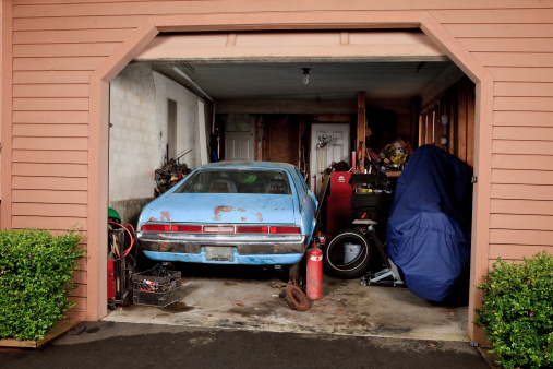 Crowded dirty garage with old car, motorcycle and many tools. 