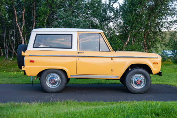 An orange colored first generation Ford Bronco is parked on a driveway in Reykjahlid, Iceland in the evening.