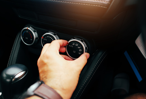The driver hand adjusts the wind direction switch on a car air conditioning dashboard, turning button switch of a car air conditioning on a switch panel control.
