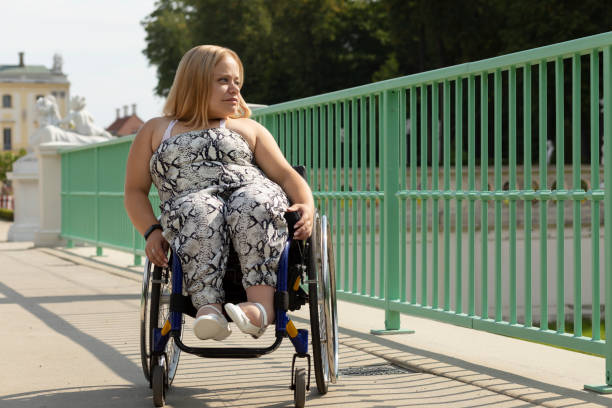 piękna młoda kobieta o niskim wzroście spaceruje po moście na wózku inwalidzkim w mieście w letni dzień. dorosła kobieta niepełnosprawna. skopiuj miejsce na tekst. płaszczyzna pozioma - achondroplazja obrazy zdjęcia i obrazy z banku zdjęć