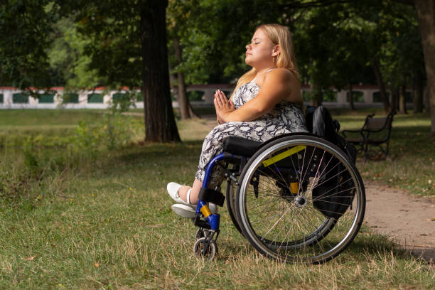 młoda kobieta o niskim wzroście na wózku inwalidzkim medytuje, relaksując się w zielonym parku w letni dzień. pełnowymiarowa dorosła kobieta z niepełnosprawnością lubi spędzać czas na łonie natury. płaszczyzna pozioma - achondroplazja obrazy zdjęcia i obrazy z banku zdjęć