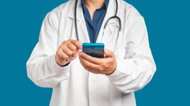 istock Doctor in a uniform with a stethoscope using a smartphone while standing on a blue background 1649920685