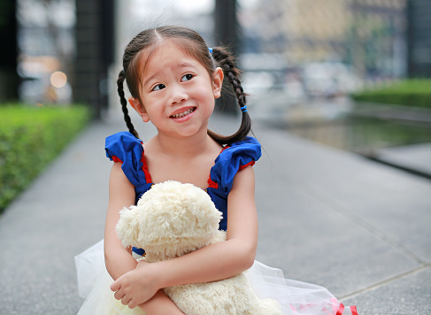 Cute little asian girl dressed with a fantasy outfit sitting in the garden with teddy bear.