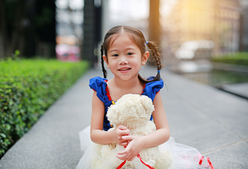 Cute little asian girl dressed with a fantasy outfit sitting in the garden with teddy bear.