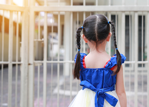 Back view of child girl holding steel fence.