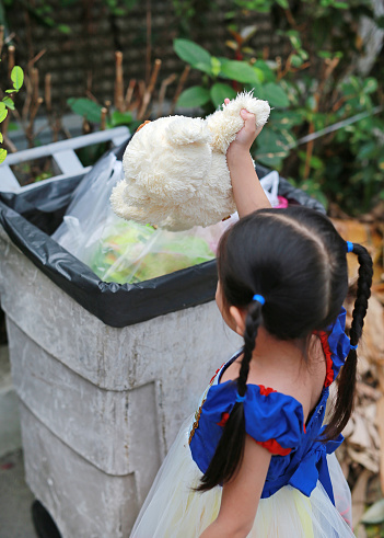 Back view if little Asian child girl dressed a fantasy outfit with keeping teddy bear from a bin.