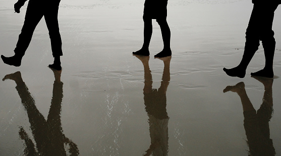 Close up silhouette foot of three young man walking on the beach in the early morning