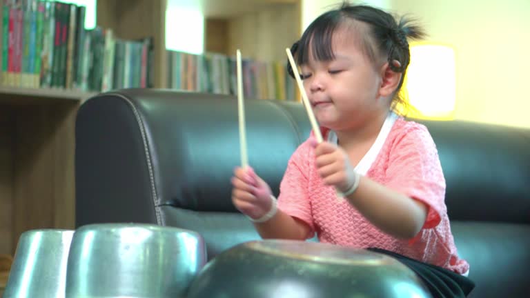 Asian little girl playing pots and pans up sofa at home .