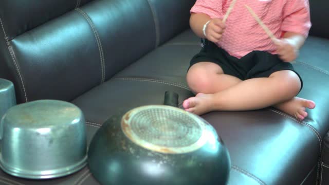 Asian little girl playing pots and pans up sofa at home .