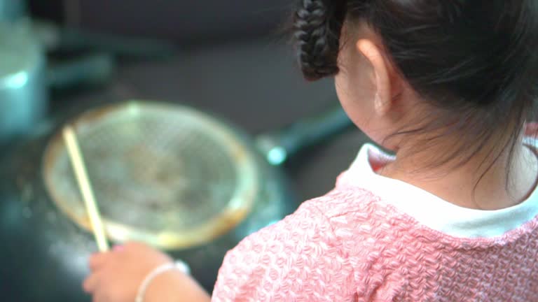 Asian little girl playing pots and pans up sofa at home .