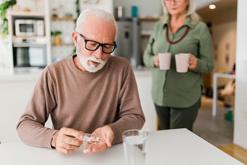 Senior Man Sitting At Home Taking Medication Pills From Bottle