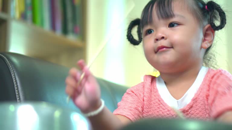 Asian little girl playing pots and pans up sofa at home .