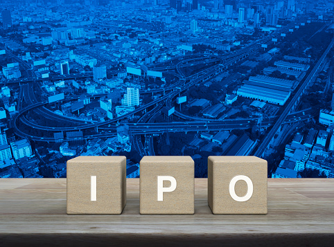 IPO letter on wood block cubes on wooden table over modern office city tower, street, expressway and skyscraper, Initial public offering concept