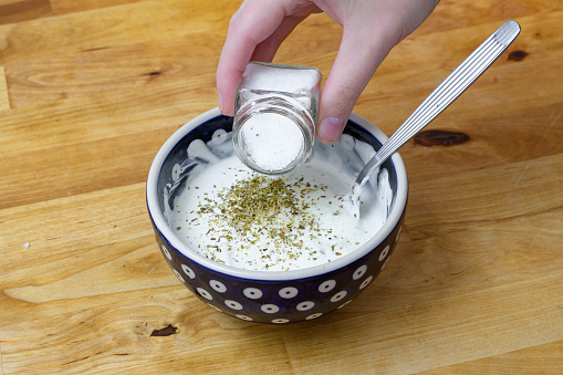 Season the white sauce in a bowl with salt and herbs, closeup