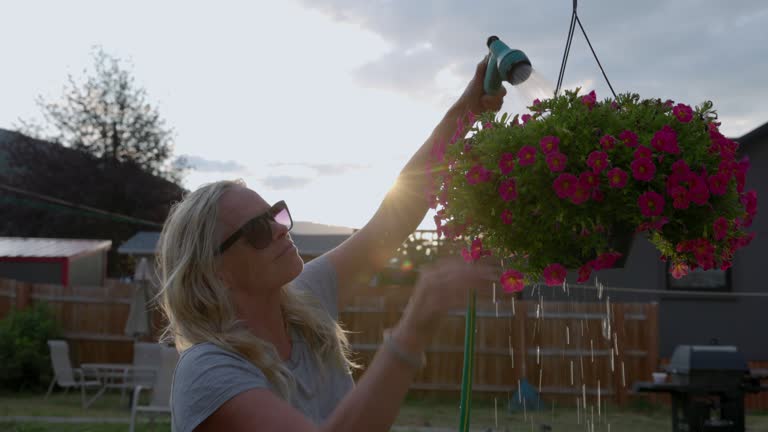 Mature woman waters hanging planter in back yard