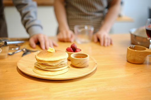 Tasty homemade pancakes with butter and maple syrup on wooden plate.