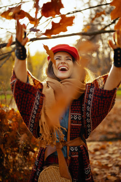 joven sonriente con sombrero rojo lanzando hojas de otoño - autumn women leaf scarf fotografías e imágenes de stock