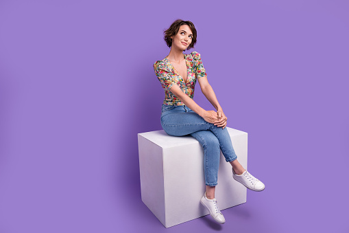Full length photo of minded lovely person sit podium cube look empty space contemplate isolated on violet color background.