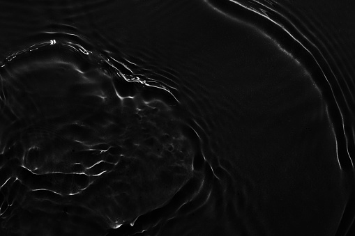 Water black surface abstract background. Waves and ripples texture of cosmetic aqua moisturizer with bubbles