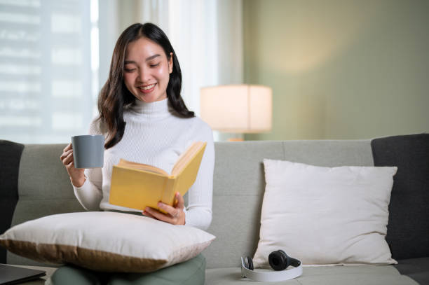 istock A beautiful Asian woman enjoys reading a book while having her morning coffee on a sofa 1650188695