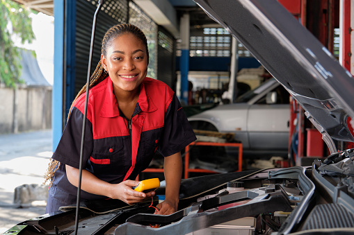 One Black female professional automotive mechanical worker checks an EV car battery and hybrid engine at a maintenance garage, expert electric vehicle service, and fixing occupations auto industry.