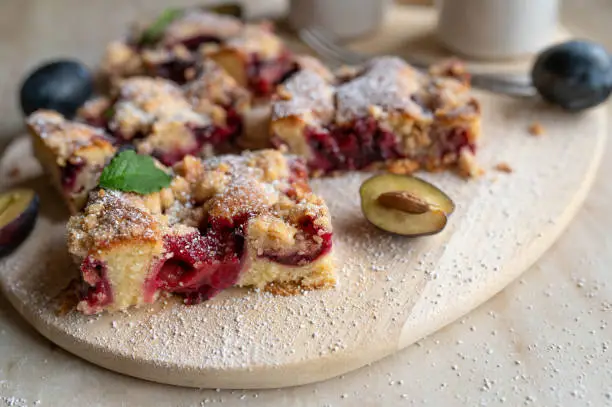 Traditional german plum cake with crumbles. Served sliced on a light wooden cutting board. Closeup, front view, selective focus