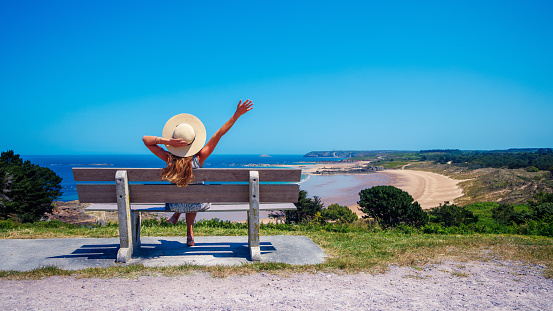 Happy woman sitting on a bench looking at the sea- vacation, travel destination, relaxing concept