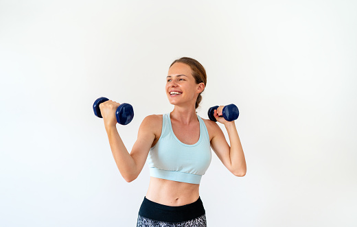 Sports lifestyle female athlete posing with dumbbells in her hands in front of white background in studio and smiling.