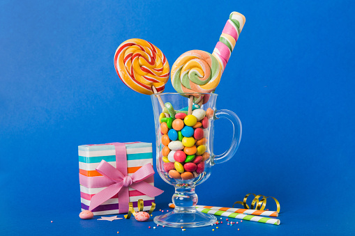 Colorful candies in cup on table on light background background. Large swirled lollipops. Creative concept of a jar full of delicious sweets from the candy store.
