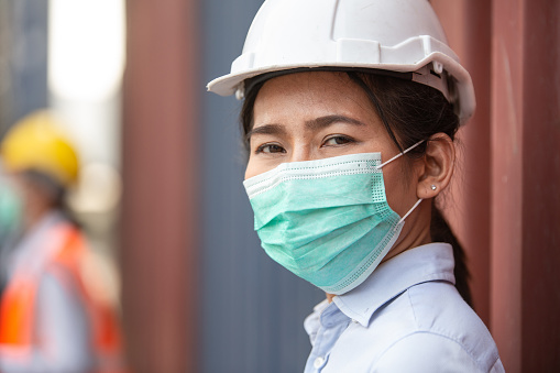 Asian woman worker wearing protective mask working at logistic cargo warehouse looking at camera. Export and import business concept