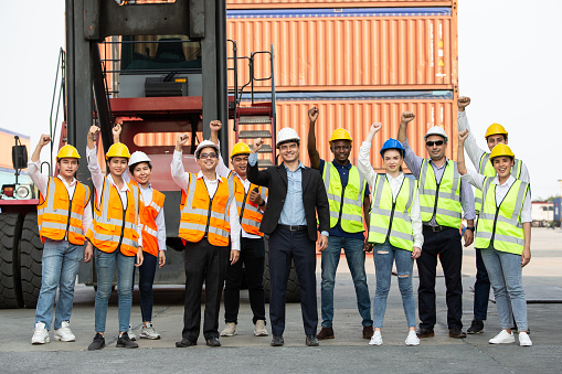Group of logistic worker lifting hands up in the air for successful work or project at container warehouse. Export import business, company teamwork