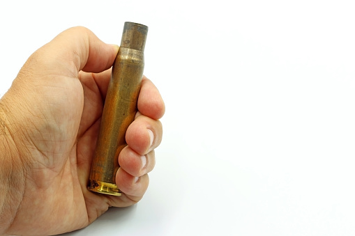 A hand showing a large-caliber bullet casing. Space for text