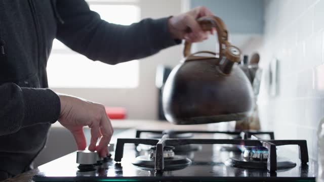 Woman turning on a gas burner stove to boil water in a kettle
