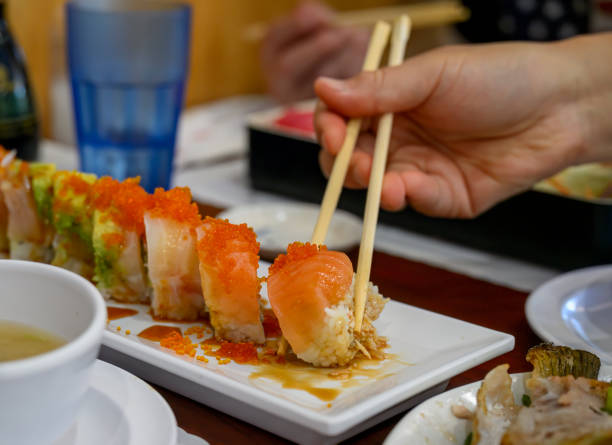Human hands holding chopsticks and picking Salmon Sushi Roll on the plate.