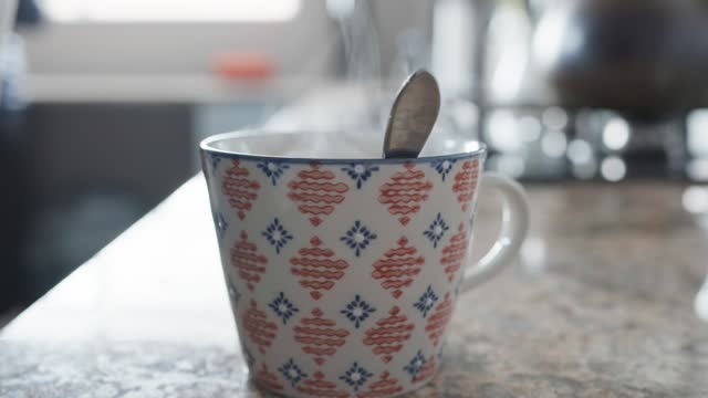 Woman steeping a teabag in a cup in her kitchen
