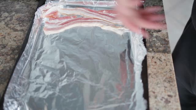 Woman laying bacon strips on a baking tray while making breakfast