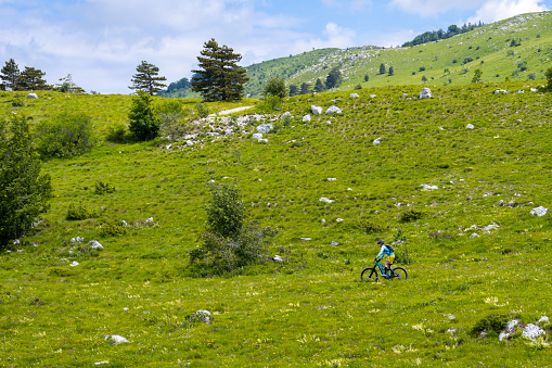 Side view of mature woman mountain biking on grassy landscape.
