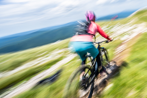 Blurred motion of rear view of mature woman riding electric bicycle against sky.