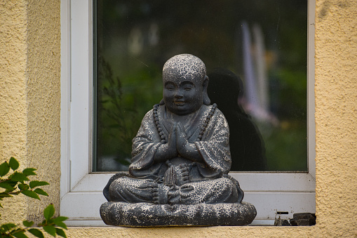 An old Budha statue placed in front of a window