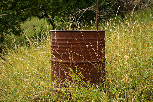 An old rusted barrel left in the field with some tall grass