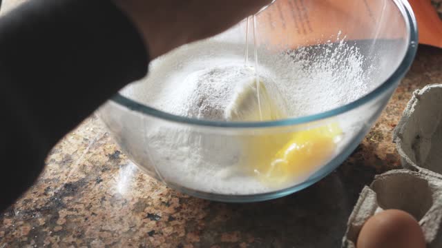 Woman cracking an egg into a bowl of flour while making breakfast